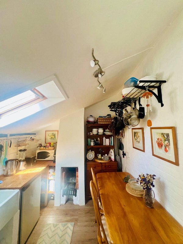 Bright kitchen and dining area with wooden table, wall shelves, framed art, and skylight window