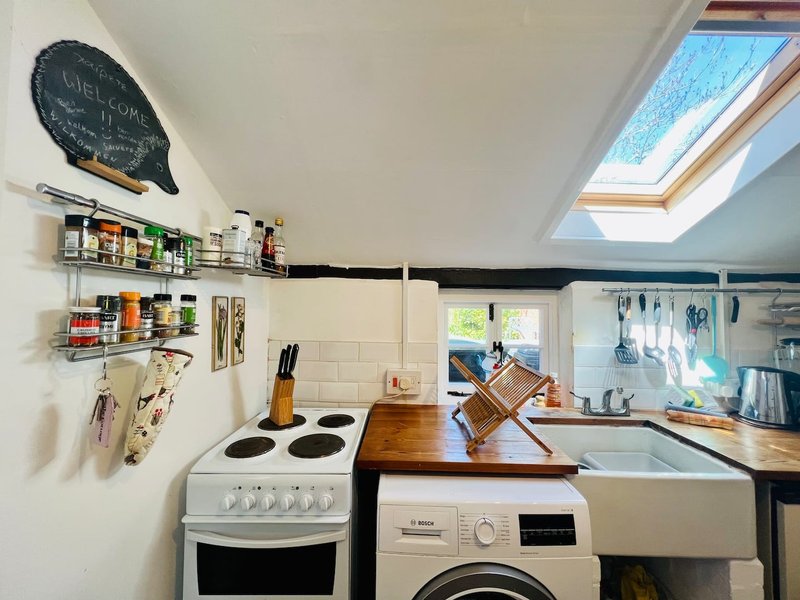 Compact kitchen with electric cooker, washing machine, open shelving and skylight window
