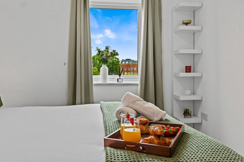 Bright bedroom with bed, green throw, wooden tray with drinks and window view of garden
