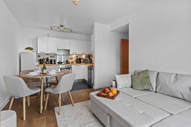 Open-plan living area with kitchen, dining table, and grey sofa with cushions