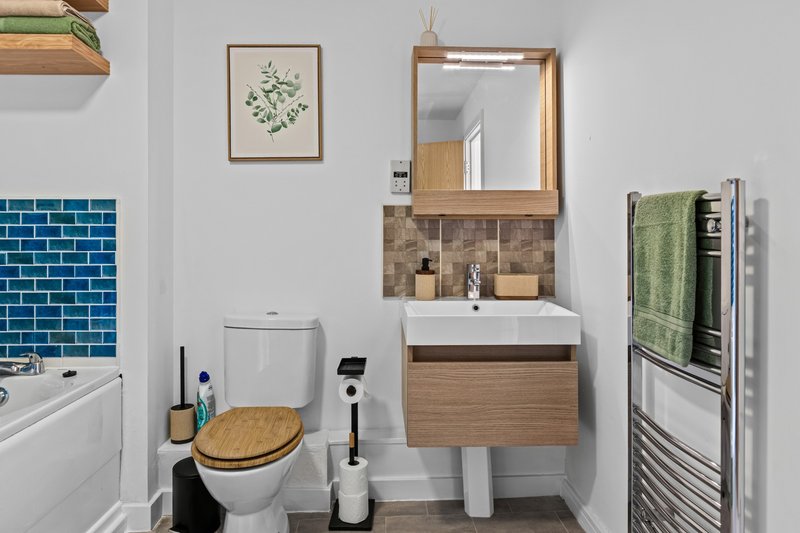 Modern bathroom with toilet, wooden vanity, mirror, heated towel rail and teal tile splashback