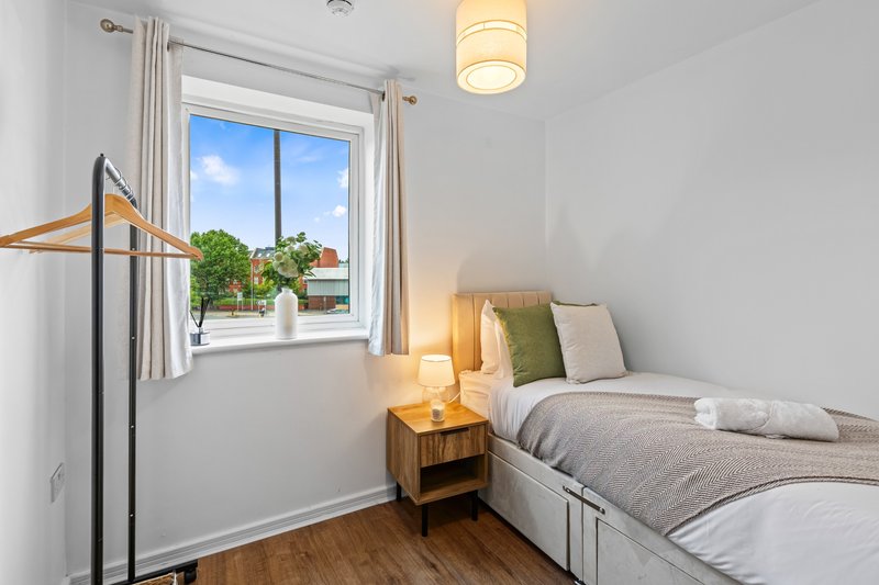 Bright bedroom with single bed, wooden nightstand, potted plant and window with outdoor view