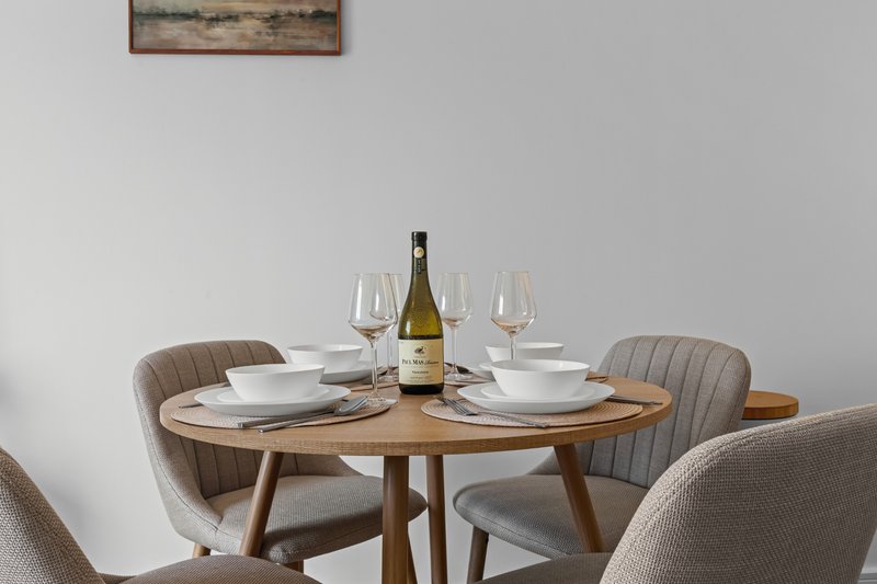 Dining table set for two with wine bottle, glasses, plates and upholstered chairs