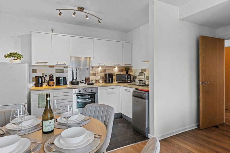 Modern kitchen with white cabinetry, wooden dining table set with plates and wine bottle
