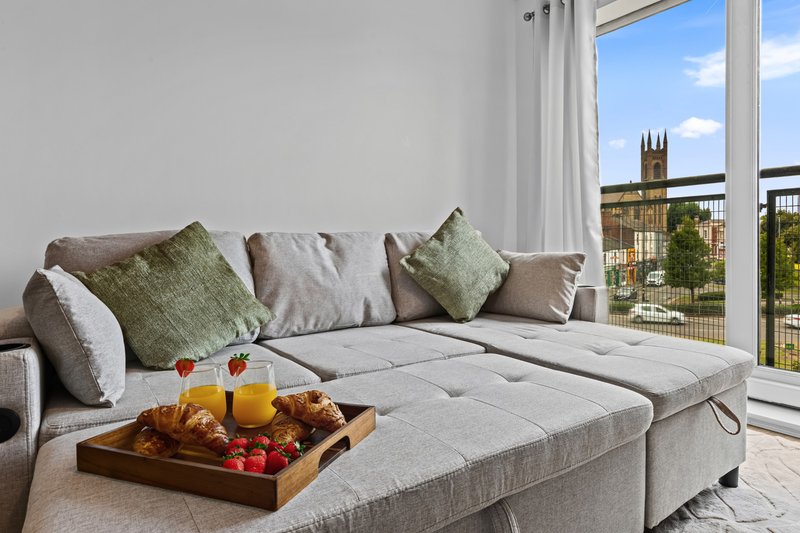 Modern living room with gray sofa, green cushions, wooden tray with fruit and juice on seat