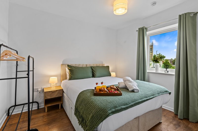 Bright bedroom with double bed, green bedding, wooden floor and large window with garden view