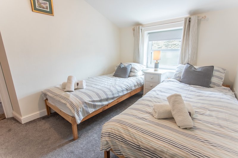 Bright twin bedroom with two single beds, striped bedding, pillows and window with curtains