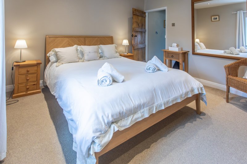 Spacious bedroom with wooden bed frame, white bedding, rolled towels, bedside lamps and mirror