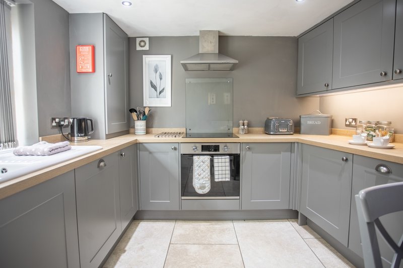 Modern kitchen with gray cabinetry, wooden worktops, integrated appliances and tiled flooring