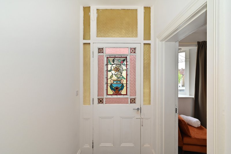 Hallway with white door, stained glass window insert, and gold-framed artwork above