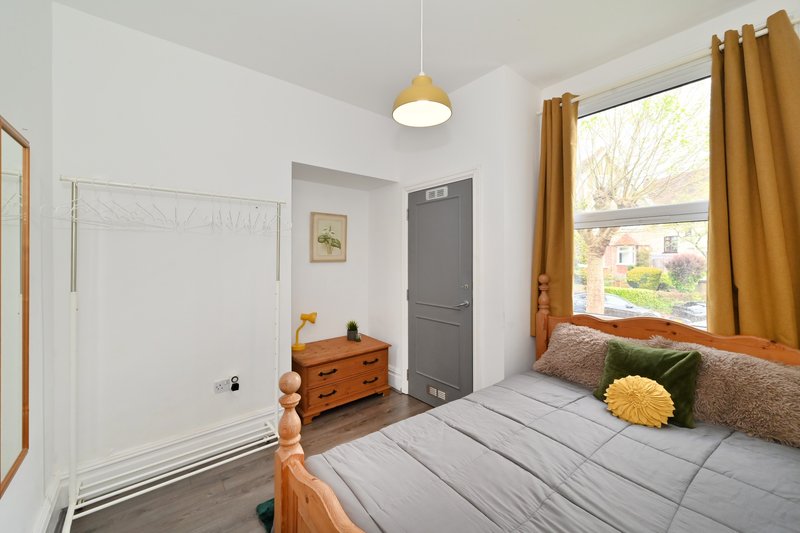 Bright bedroom with double bed, wooden dresser, window with gold curtains and street view