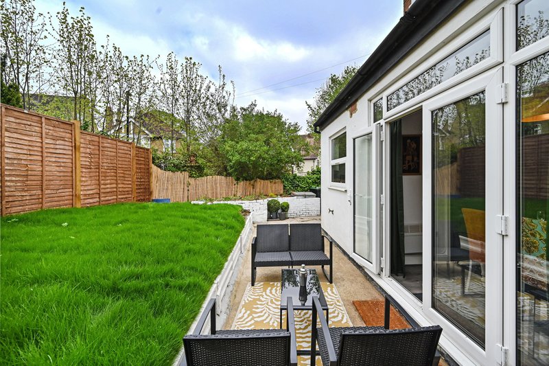 Spacious garden with patio area, modern white conservatory, wooden fencing and green lawn
