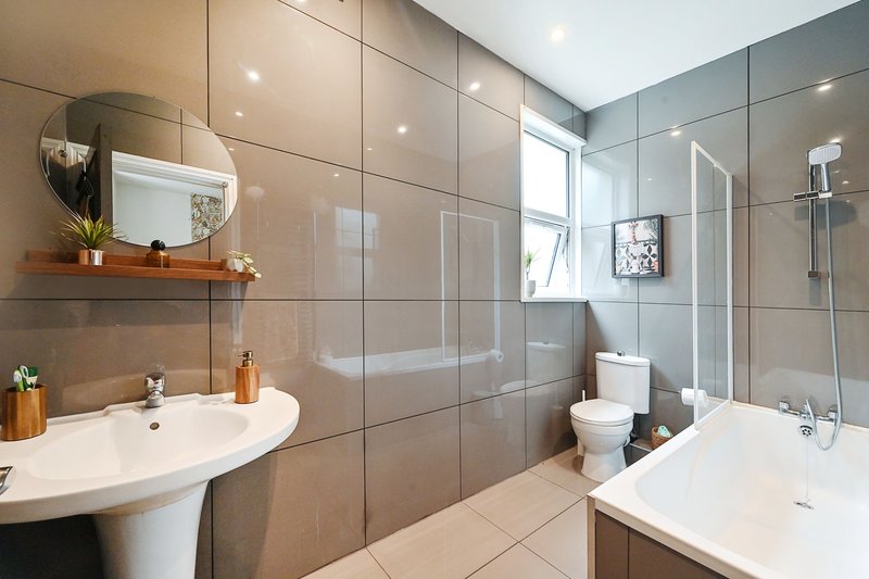 Modern bathroom with dual sinks, large mirror, walk-in shower and tiled walls