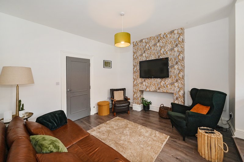 Living room with brown leather sofa, black armchair, wall-mounted TV, and gold pendant light