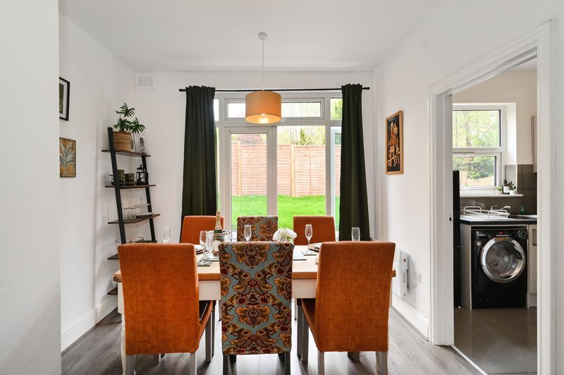 Dining room with white table, orange upholstered chairs, black curtains, and garden view
