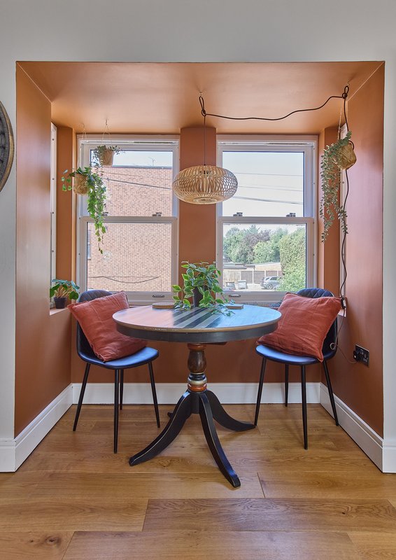 Cozy nook with round table, two chairs with red cushions, plants and woven pendant lights