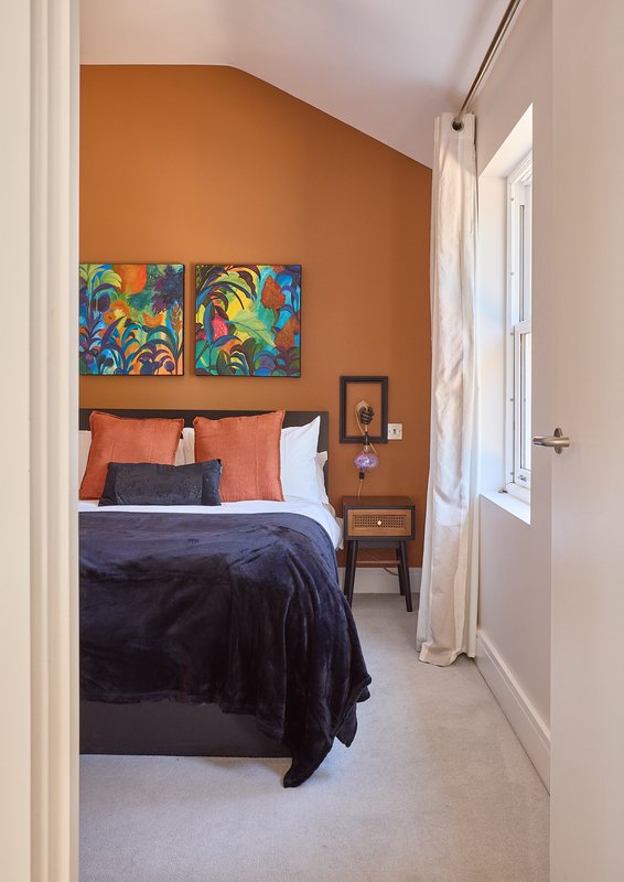 Bedroom with orange accent wall, double bed, colorful artwork, and wooden nightstand