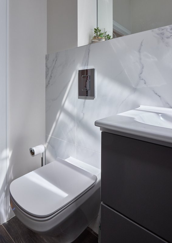 Modern bathroom with white toilet, marble-effect wall tiles, and dark vanity unit
