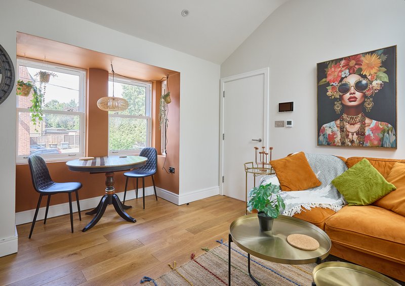 Open-plan living room with orange sofa, dining area by window, wooden flooring and colorful wall art