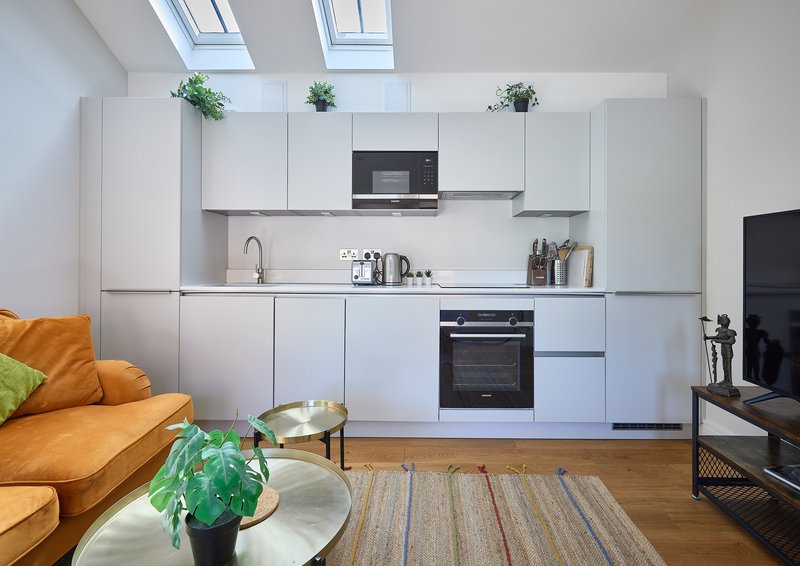 Modern kitchen with white cabinetry, integrated appliances, and open-plan living area with orange sofa