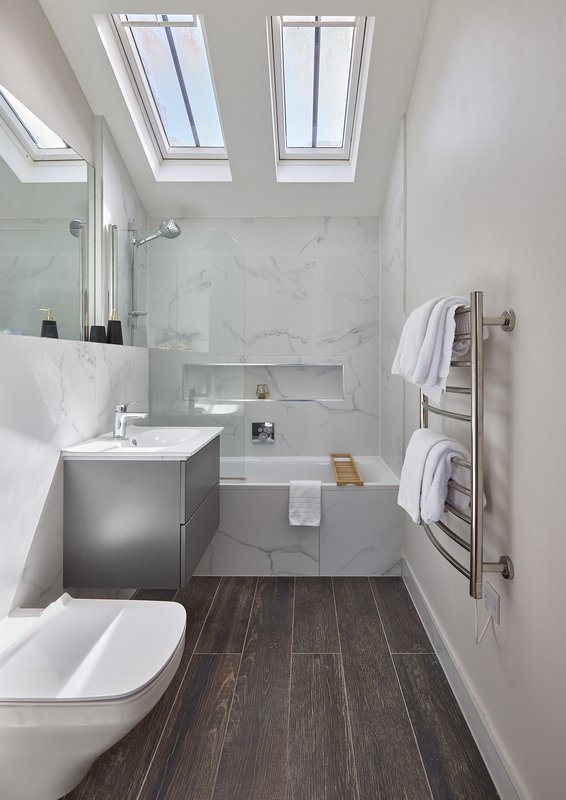 Modern bathroom with skylight, marble shower enclosure, dark wood flooring and heated towel rail