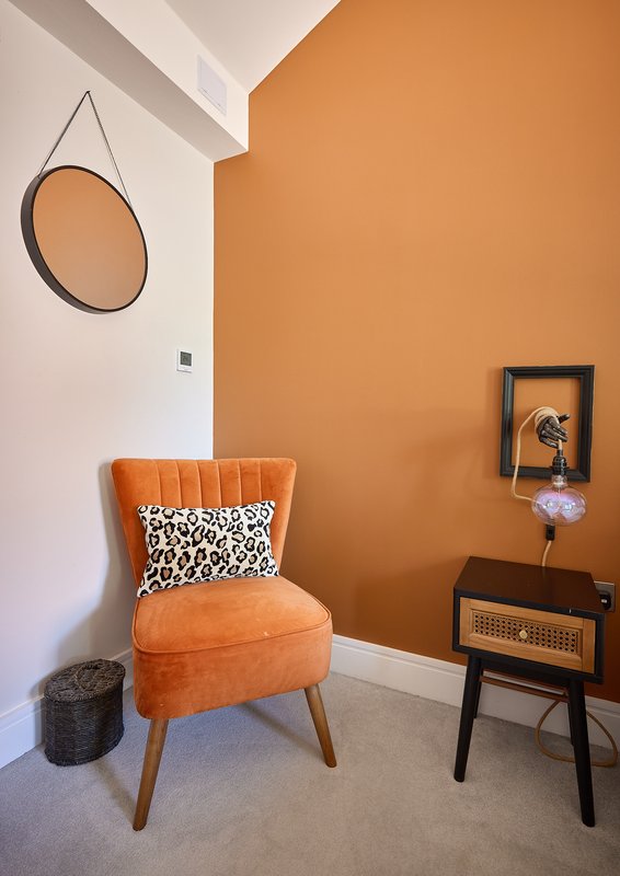Modern bedroom corner with orange accent wall, mid-century chair, round mirror and side table