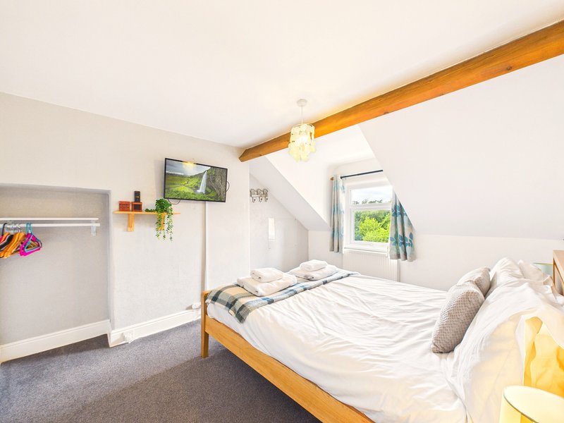 Bright bedroom with wooden beam, double bed, white bedding, and window with countryside view