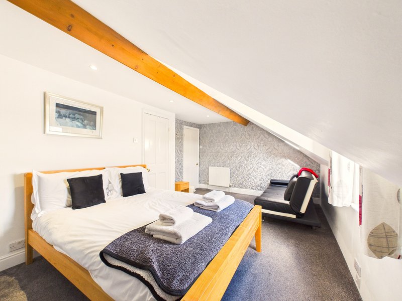 Attic bedroom with wooden bed, white bedding, black cushions, and exposed beam