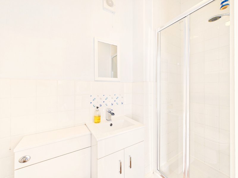 Clean white bathroom with vanity sink, mirror, toilet and shower enclosure