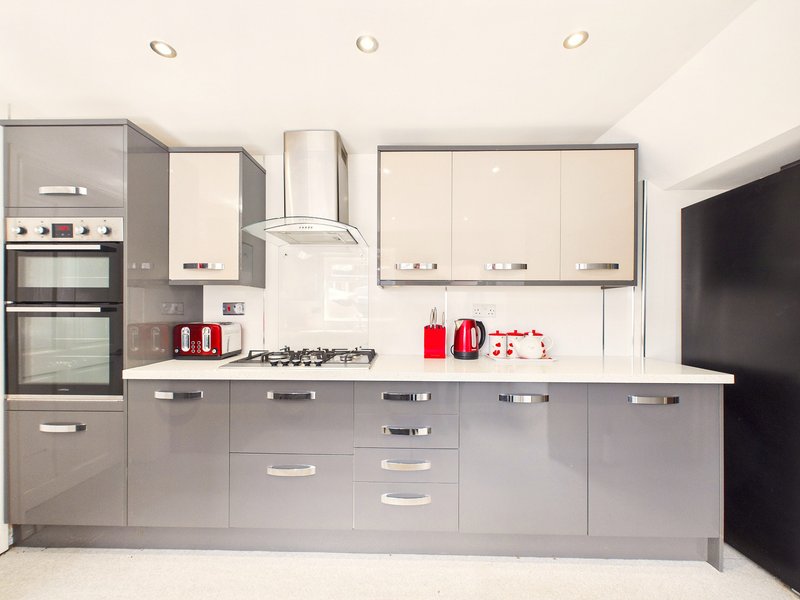 Modern kitchen with grey and white cabinetry, integrated appliances, and red kettle and toaster on countertop