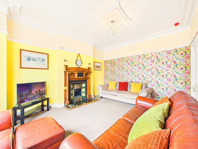 Bright living room with colorful sofas, fireplace, TV, and floral wallpaper accent wall