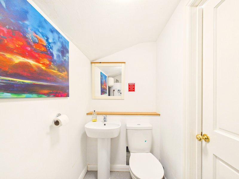 Compact bathroom with pedestal sink, toilet, artwork and mirror