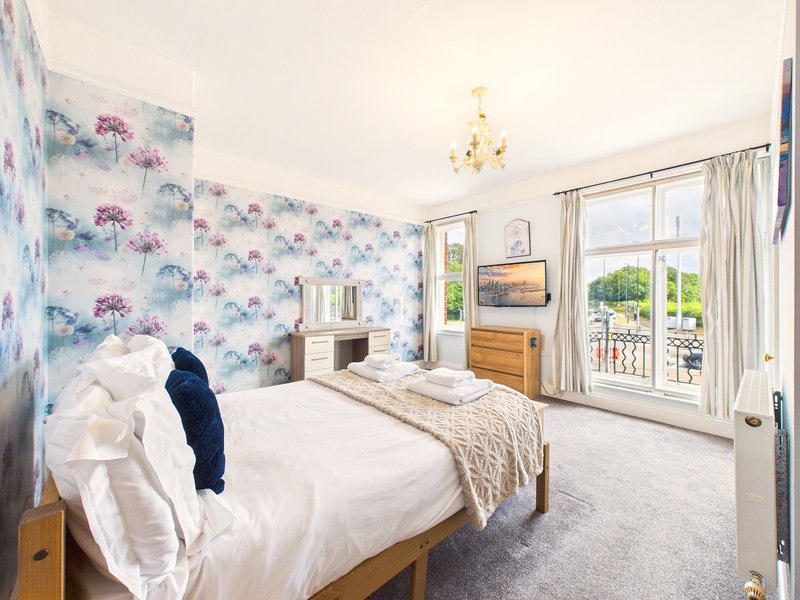 Bright bedroom with floral wallpaper, double bed, wooden furniture and patio doors to balcony