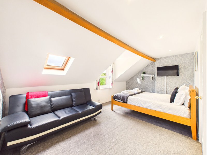 Attic bedroom with skylight, black leather sofa, wooden bed frame and neutral carpeting