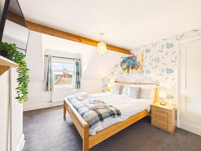 Bright bedroom with wooden bed, floral wallpaper, exposed beam, and window with countryside view