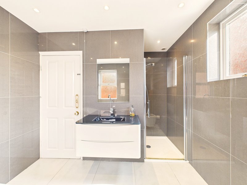 Modern bathroom with gray tile walls, white vanity, mirror, and walk-in shower