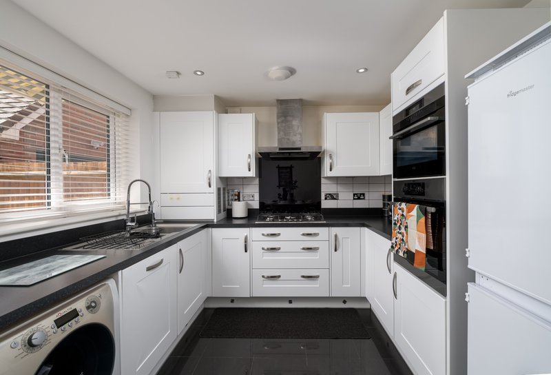 Modern kitchen with white cabinetry, black countertops, gas hob, and integrated appliances