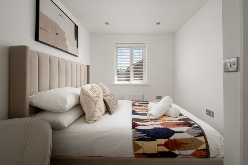 Modern bedroom with upholstered headboard, white bedding, throw blankets, and window with shutters