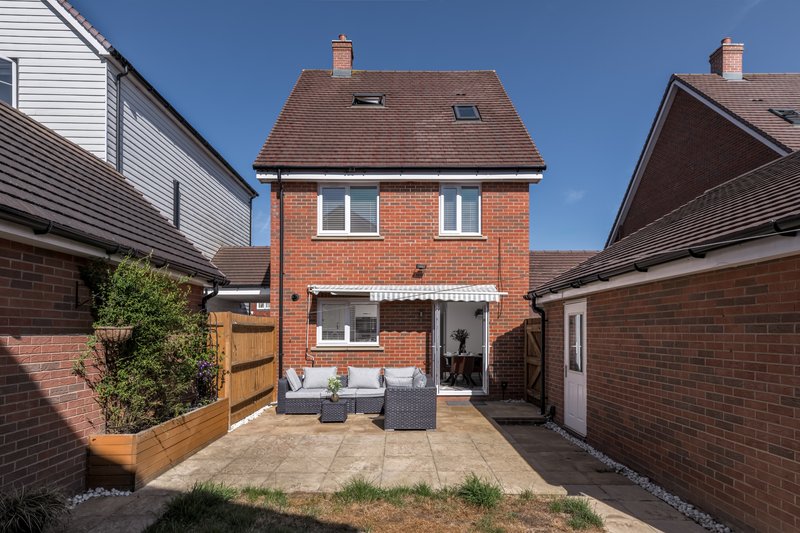 Brick house exterior with patio area, garden seating, and neighboring properties visible