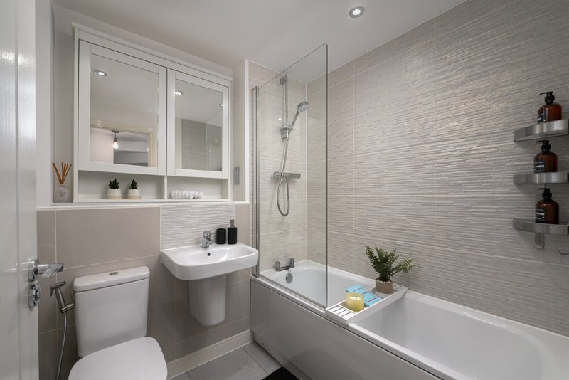 Modern bathroom with toilet, pedestal sink, mirror cabinet, tiled walls and bathtub