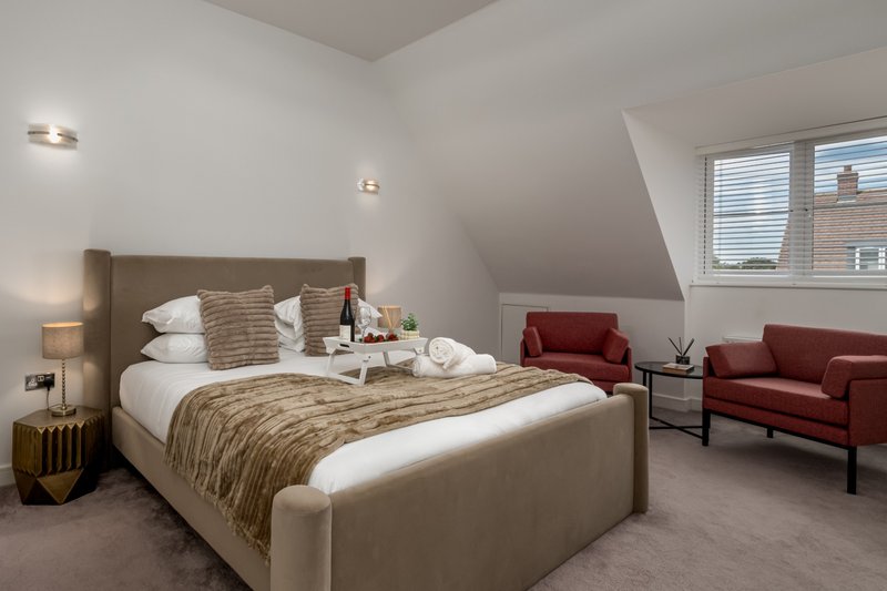 Spacious bedroom with upholstered bed, red armchair, sloped ceiling and windows