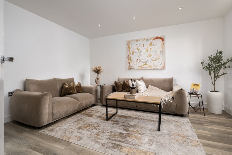 Spacious living room with gray sofas, wooden table, framed artwork, and potted plant