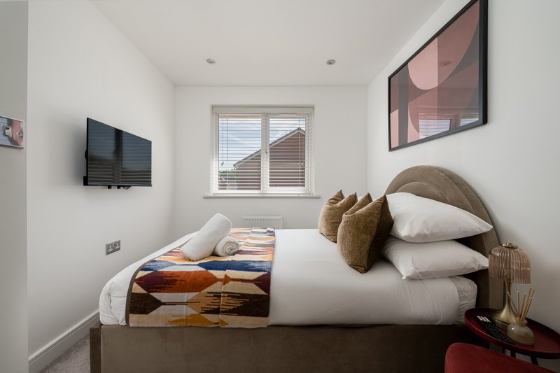 Modern bedroom with double bed, wall-mounted TV, window with shutters and bedside decor