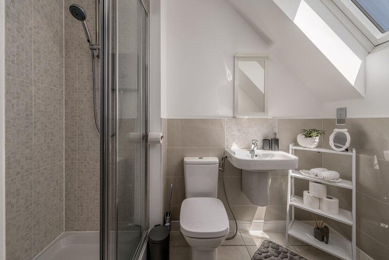 Modern bathroom with shower enclosure, toilet, sink and white shelving unit
