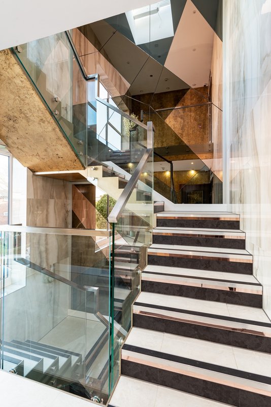 Modern spiral staircase with glass railings, wooden steps and metal handrail in bright interior