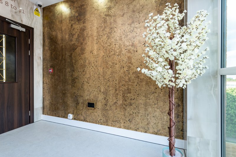 Modern hallway with textured bronze wall, white flowers in vase, and wooden door