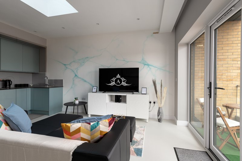 Modern living room with sofa, TV wall, kitchen area and glass doors to garden