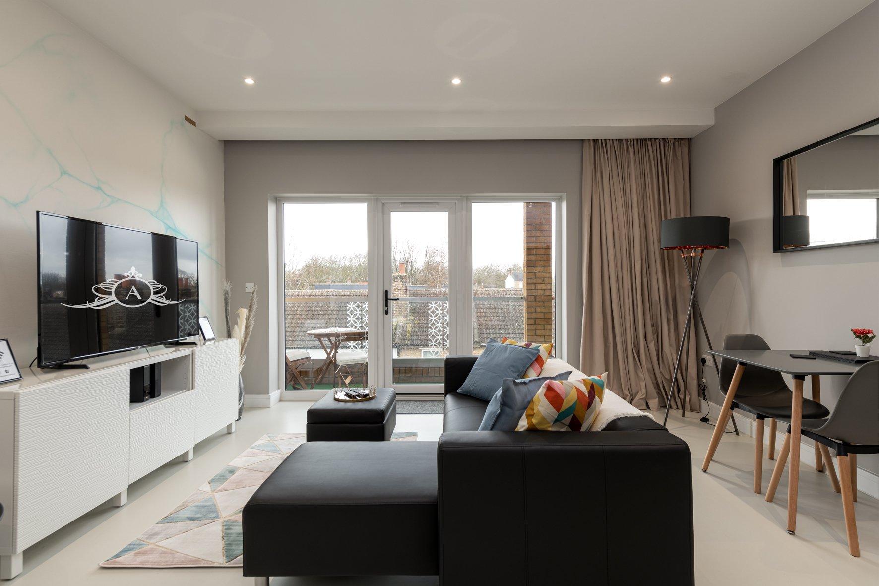 Modern open-plan living room with black sofa, TV, desk, and floor-to-ceiling windows overlooking city