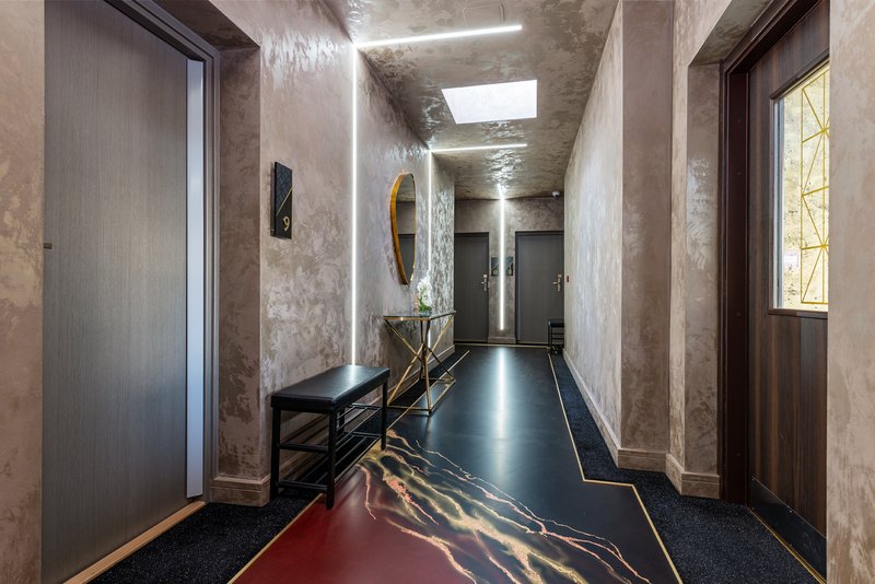 Modern hallway with concrete walls, skylight, dark flooring with gold inlay details, and wooden doors