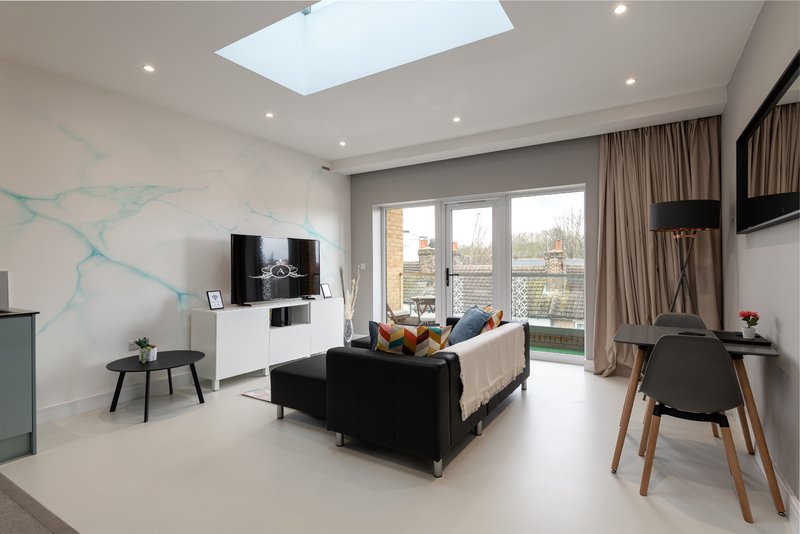 Modern open-plan living room with black sofa, TV, skylight, floor-to-ceiling windows and balcony